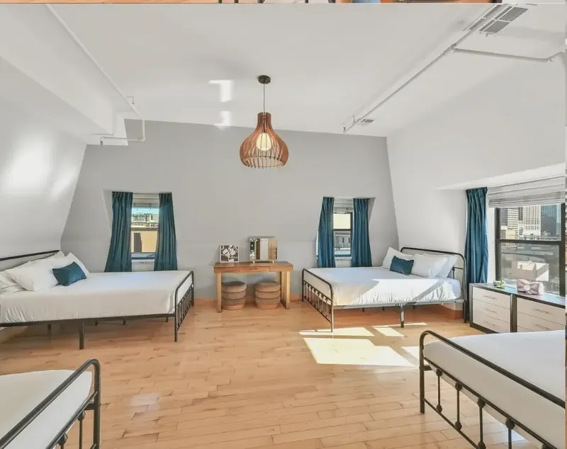 Two beds with white linens under sloped ceilings and teal curtains, on a wood floor