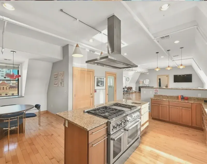 A kitchen with a large range under a steel hood, a granite island and wood floors