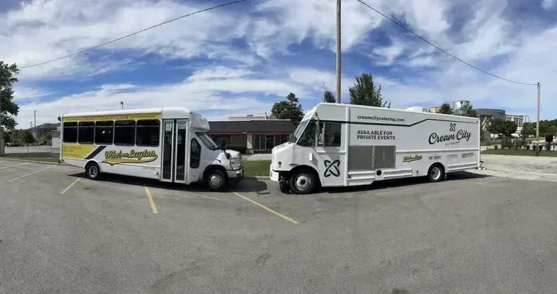 The white shuttle bus parked beside the Cream City Catering truck in a lot