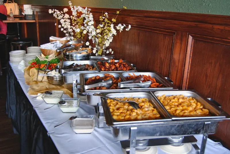A long buffet table set with chafing dishes, platters and stacked plates under warm light