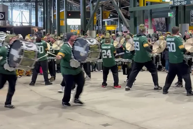 A drumline in Packers jerseys playing on the stadium concourse