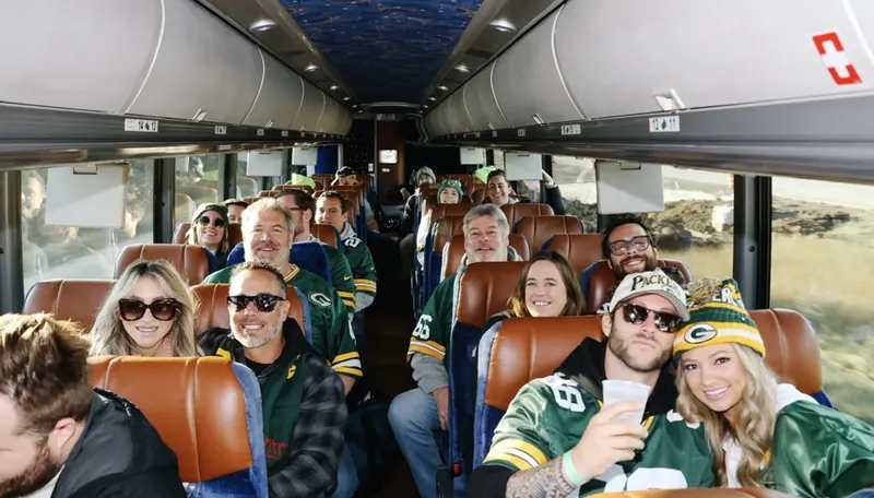 Riders in Packers gear smiling down the aisle of the coach