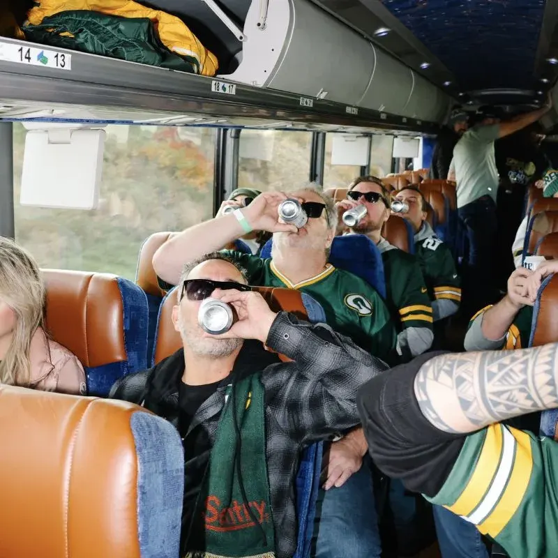 A rider in a Packers beanie and satin jacket holding up a can on the coach