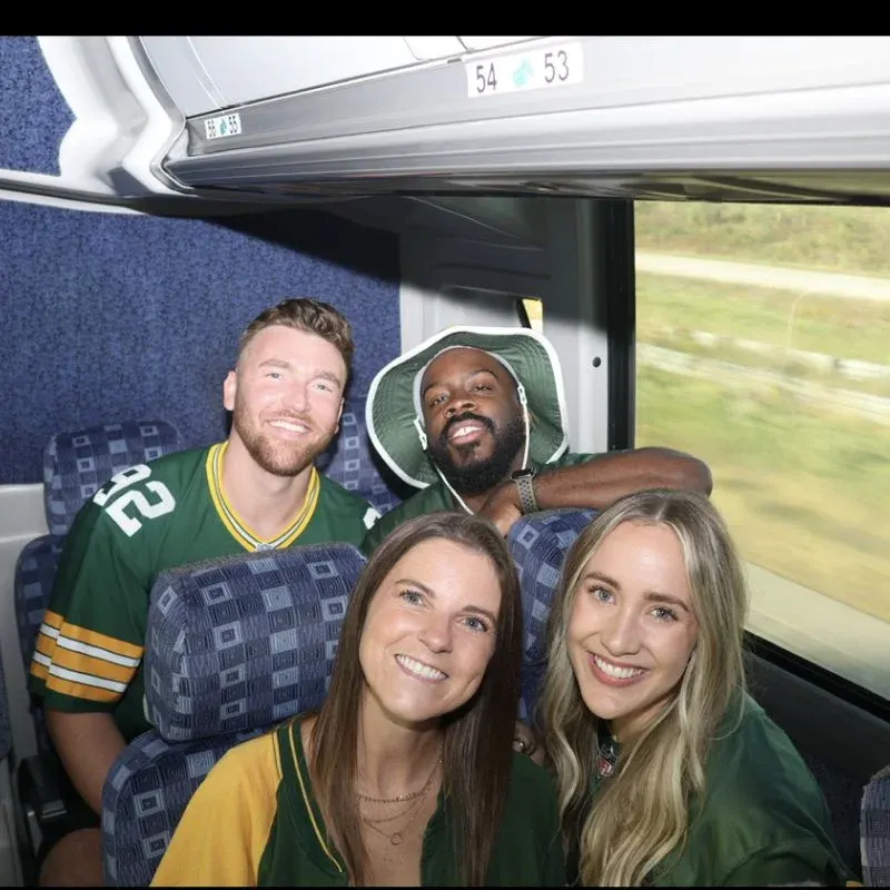 Riders in Packers jerseys posing in a window seat on the coach