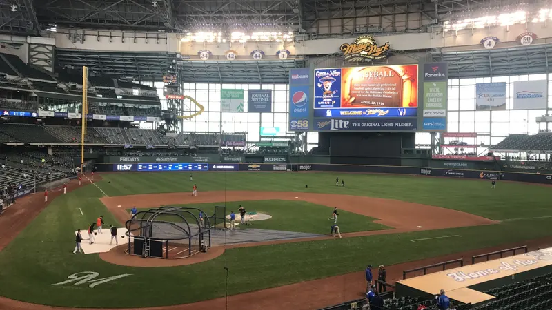 The baseball diamond at American Family Field seen from the stands, with a batting cage on the infield, the scoreboard and the stadium roof overhead