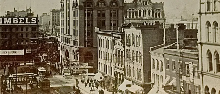 Sepia photograph of Wisconsin Street in the 1890s: the lower floors of the Pabst Building, a Gimbels sign and streetcars on the street