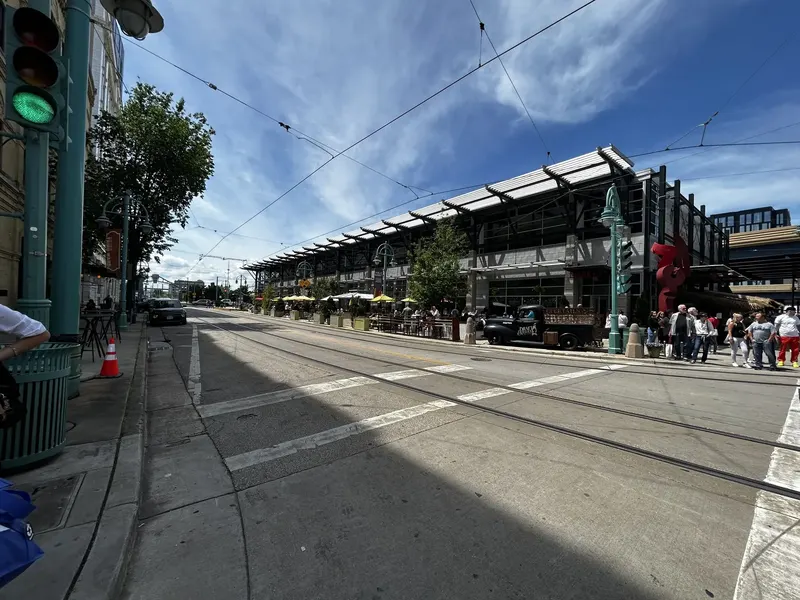 The Milwaukee Public Market, a low steel and glass hall at the end of a street with streetcar wires overhead and people outside