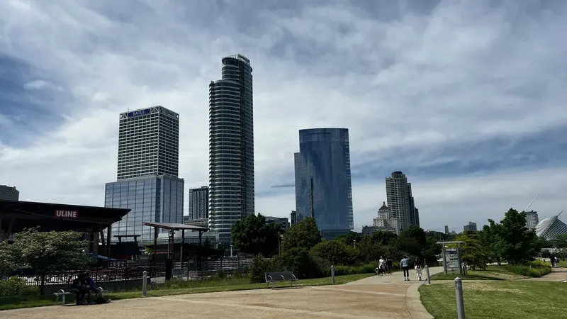 Downtown Milwaukee's towers seen across a park path from Lakeshore State Park under a cloudy sky