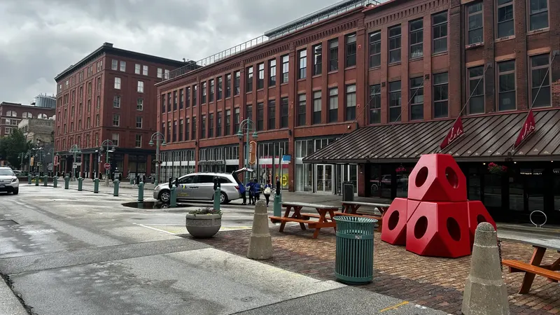 Red brick warehouse buildings in Milwaukee's Historic Third Ward, with a red geometric sculpture and picnic tables on the sidewalk