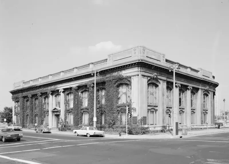 A black and white photograph of the ivy-covered Second Ward Savings Bank building with tall columns on a street corner