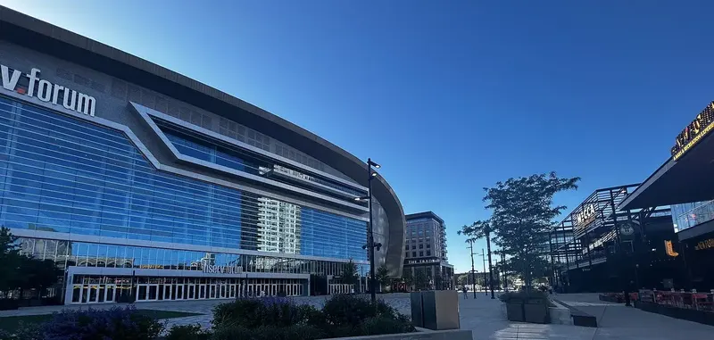 Fiserv Forum, a glass-fronted arena, under a blue evening sky with the Deer District plaza beside it