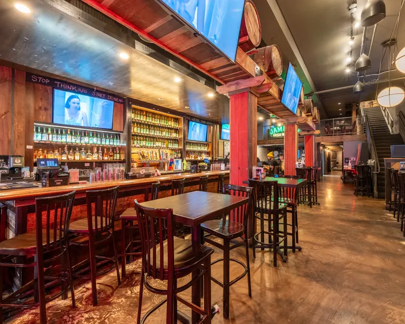 The back bar at Oak Barrel lit red, bottles on the shelves and stools along the rail