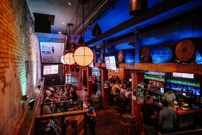 The bar at Oak Barrel Public House at night, with barrel-top lights, brick walls and a full room