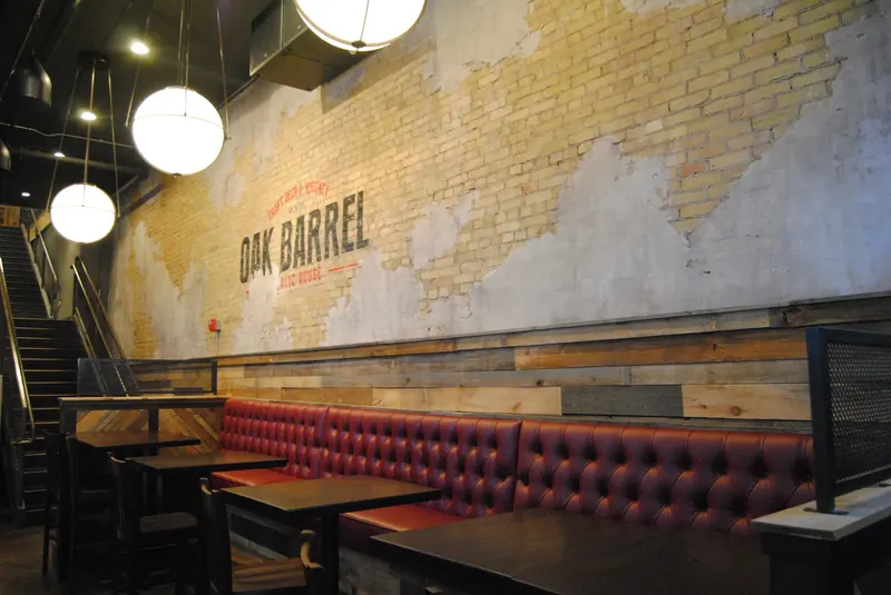 The Oak Barrel logo painted on an exposed brick wall above a row of red leather booths