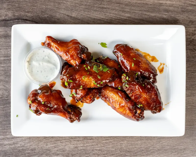 Oak Barrel signature wings glazed dark on a white plate with a cup of ranch