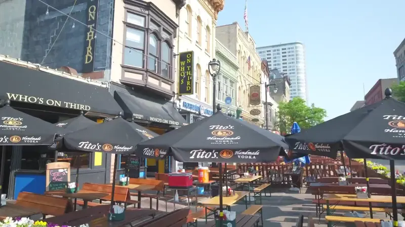The patio at Who's on Third in daylight, with picnic tables and benches under black umbrellas