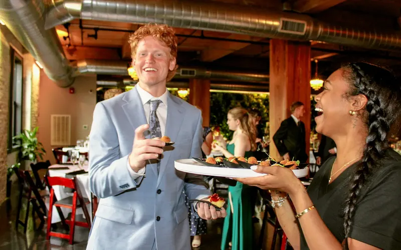 A server offering a tray of passed hors d’oeuvres to a laughing guest at a wedding reception
