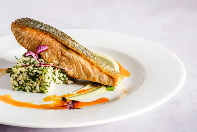 A fillet of crisp-skinned salmon over tabbouleh on a white plate