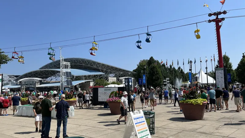 Yellow and blue gondolas of a cable ride crossing a clear blue sky above a crowd on the Henry Maier Festival Park grounds in Milwaukee