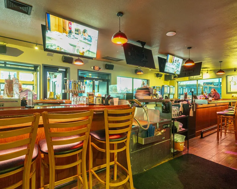 The long bar inside Who's on Layton with wooden stools, screens overhead and the kitchen window at the end