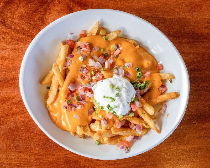 Loaded fries under cheese sauce, bacon and sour cream in a white bowl at Who's on Layton