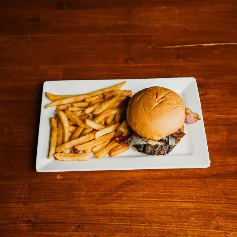 A burger on a brioche bun with fries on a white rectangular plate, on a dark wood table