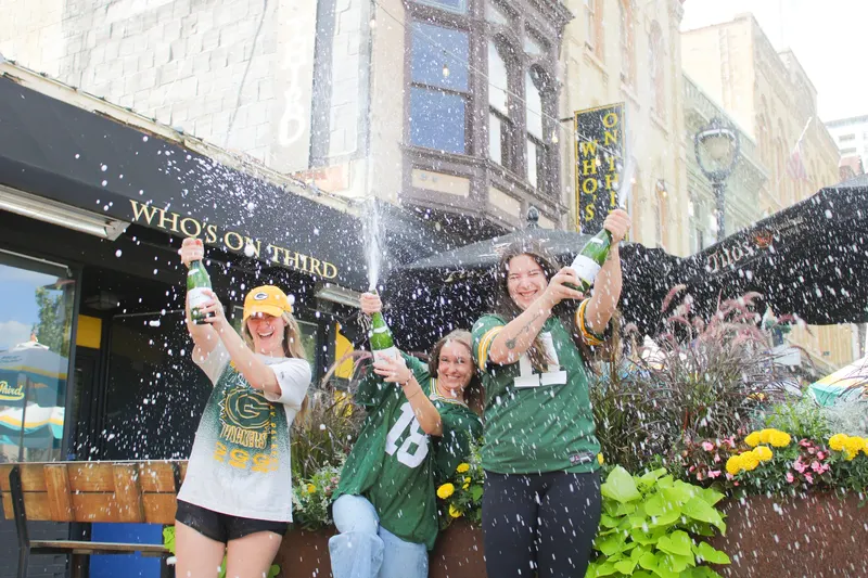 Three friends in Packers jerseys spraying champagne on the patio outside Who's on Third