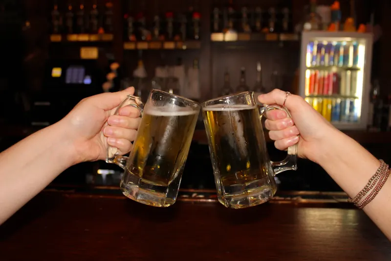 Two beer mugs clinked together in front of the back bar at Who's on Third