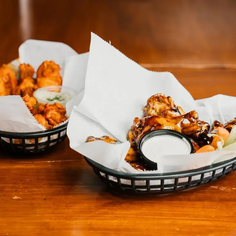 Two baskets of wings on paper liners, one with a cup of ranch dressing
